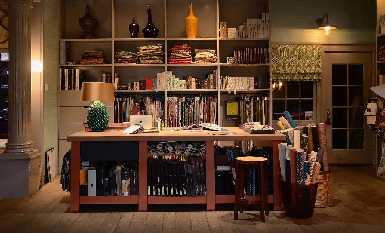 De werktafel in de studio, met een kastenwand vol stalenboeken en stoffen